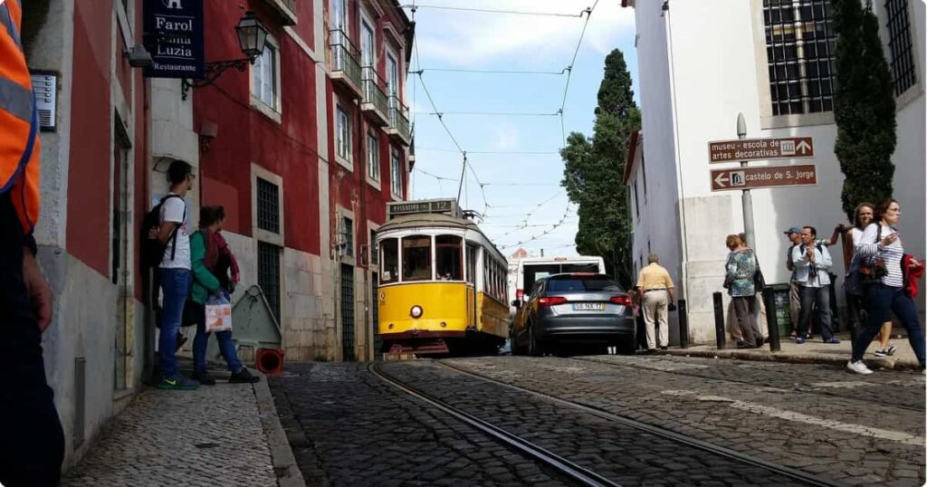 Iconic yellow tram climbing a narrow historic street in Lisbon's Alfama neighbourhood, Portugal