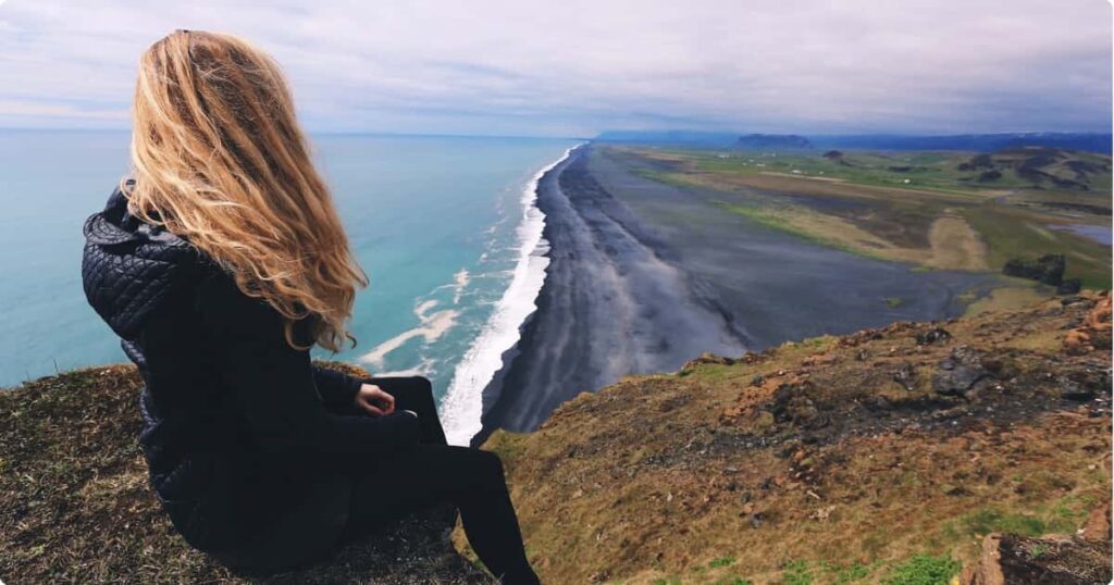 Solo female traveler sitting on coastal cliff overlooking turquoise ocean at sunrise — best destinations for solo female travel 2026