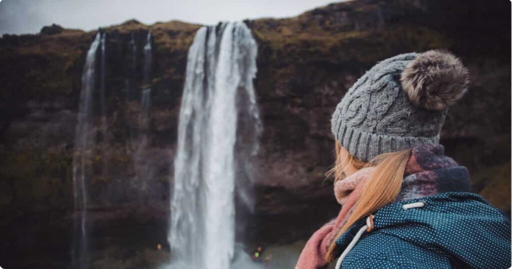 Hiker in waterproof jacket and boots standing near an Iceland waterfall in summer