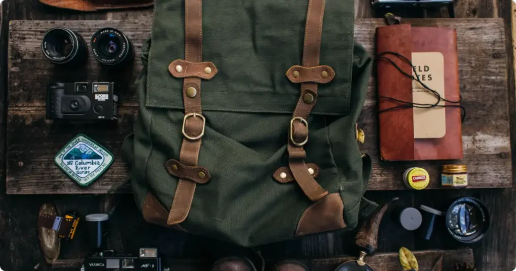 Adventure travel hiking gear flat lay with boots rain jacket dry bag and trail map on wooden table