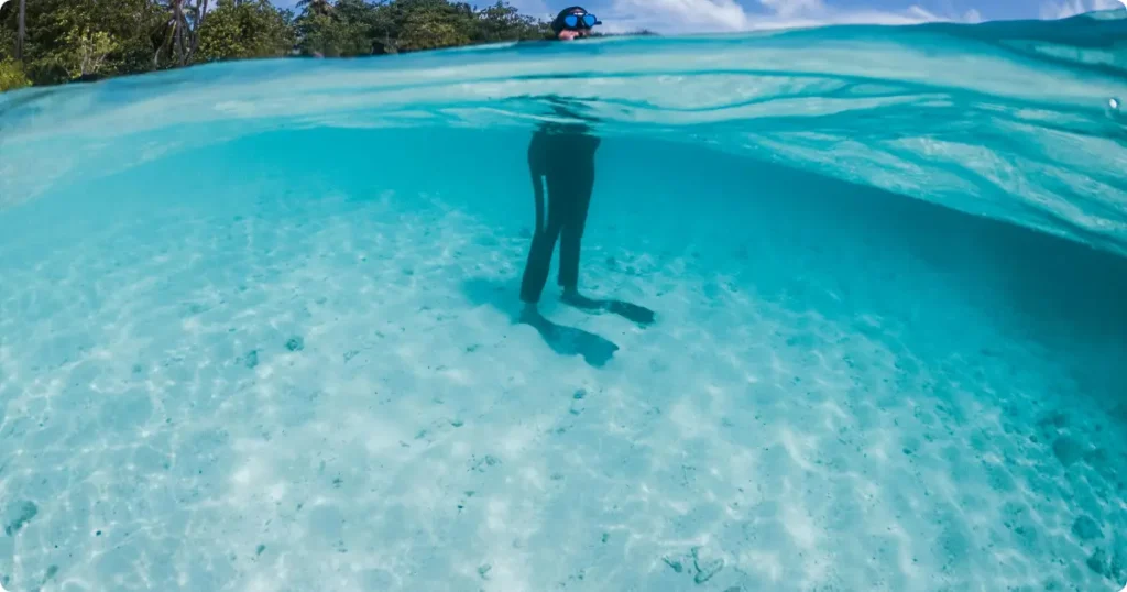 Beginner putting on snorkel mask while standing waist-deep in calm tropical water
