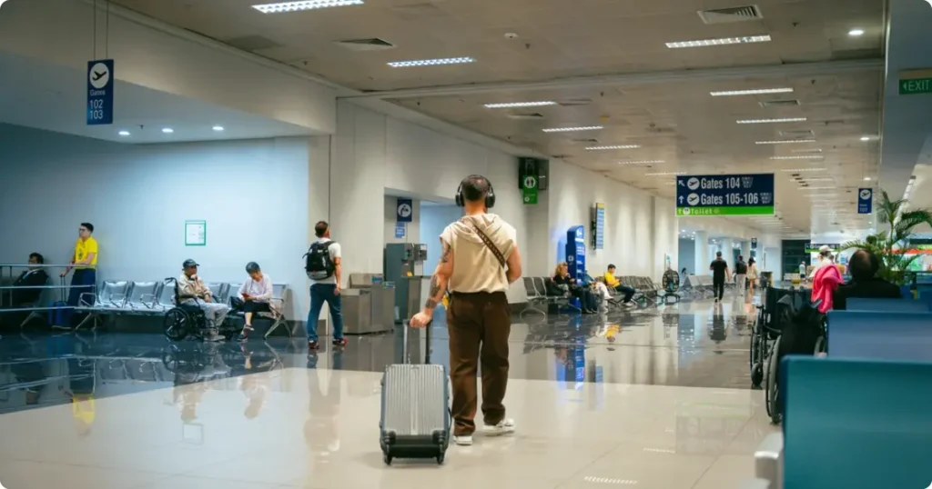 Traveller wearing noise-cancelling headphones at airport gate window before long-haul flight