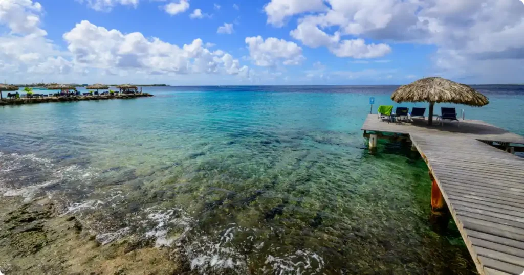 Snorkeler entering clear water at a Bonaire shore snorkel site with reef below
