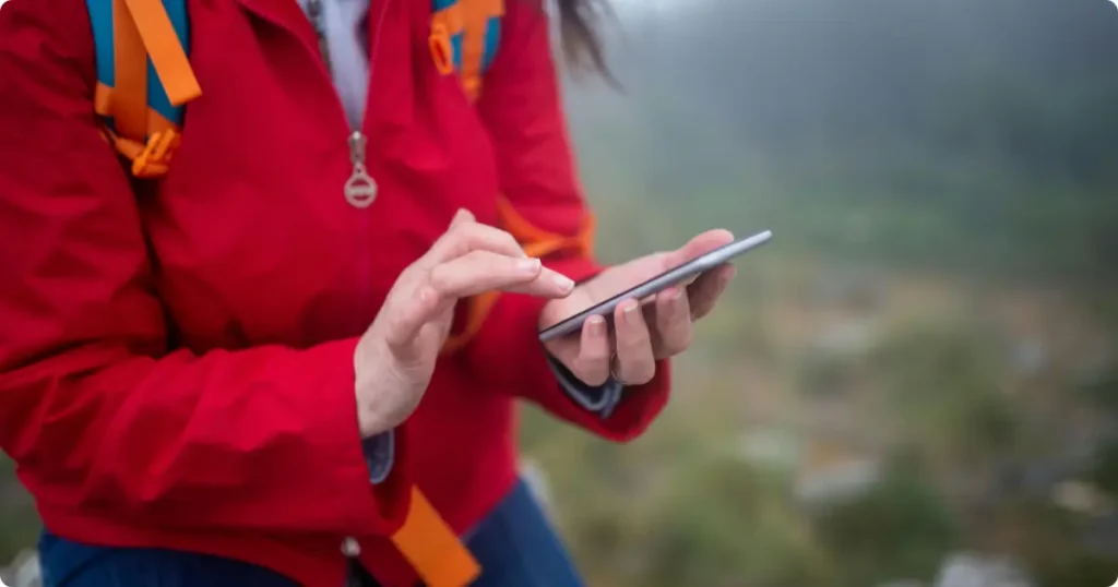 Best Outdoor Activity Apps for Hikers & Adventure Travelers Solo hiker checking outdoor activity app on smartphone while crossing an alpine mountain ridge trail