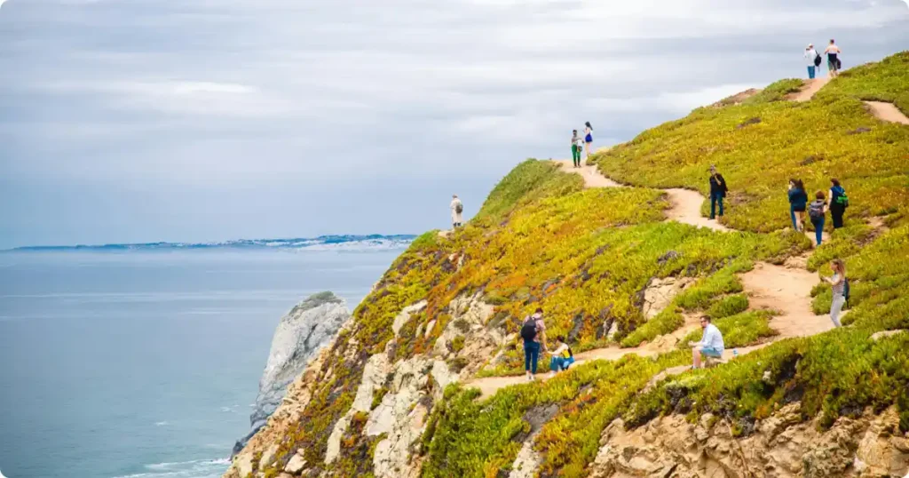 Hiker walking clifftop path on Seven Hanging Valleys Trail with turquoise ocean below Algarve
