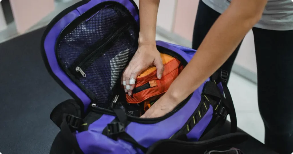 Hands packing wrapped snorkel mask into carry-on backpack with fins and mesh bag on hotel bed