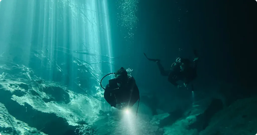 Scuba diver checking pressure gauge underwater with sunlight streaming from surface — scuba diving safety statistics