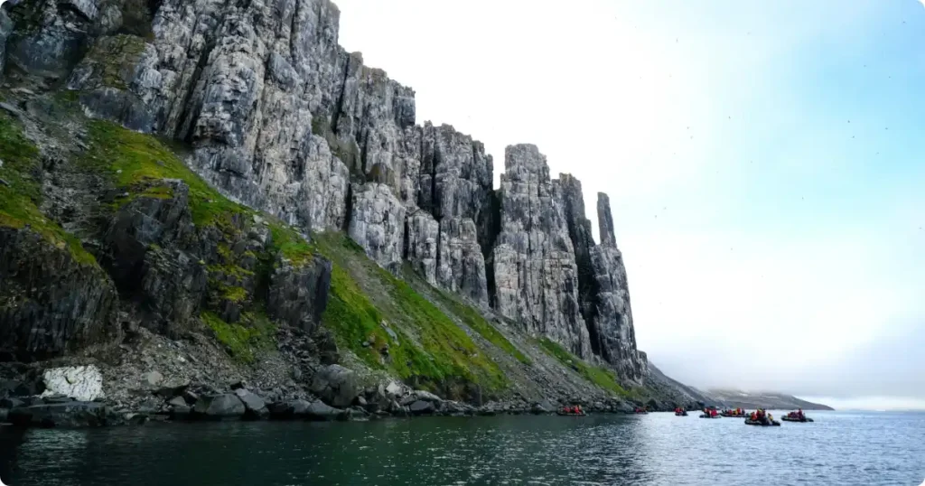 Sea kayaker beneath towering cliff faces of Lofoten Islands Norway under midnight sun