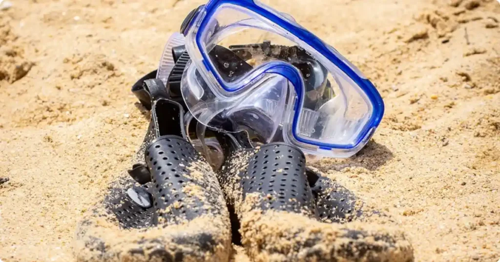 Semi-dry snorkel clipped to dive mask strap on wet sand at ocean waterline