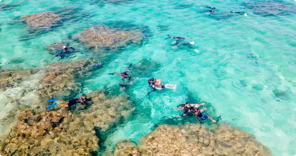 Small group snorkeling with local guide above coral reef near traditional boat in Southeast Asia