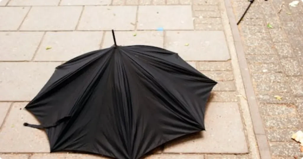 compact travel umbrella inverted in wind on wet street — why a rain jacket beats it every time