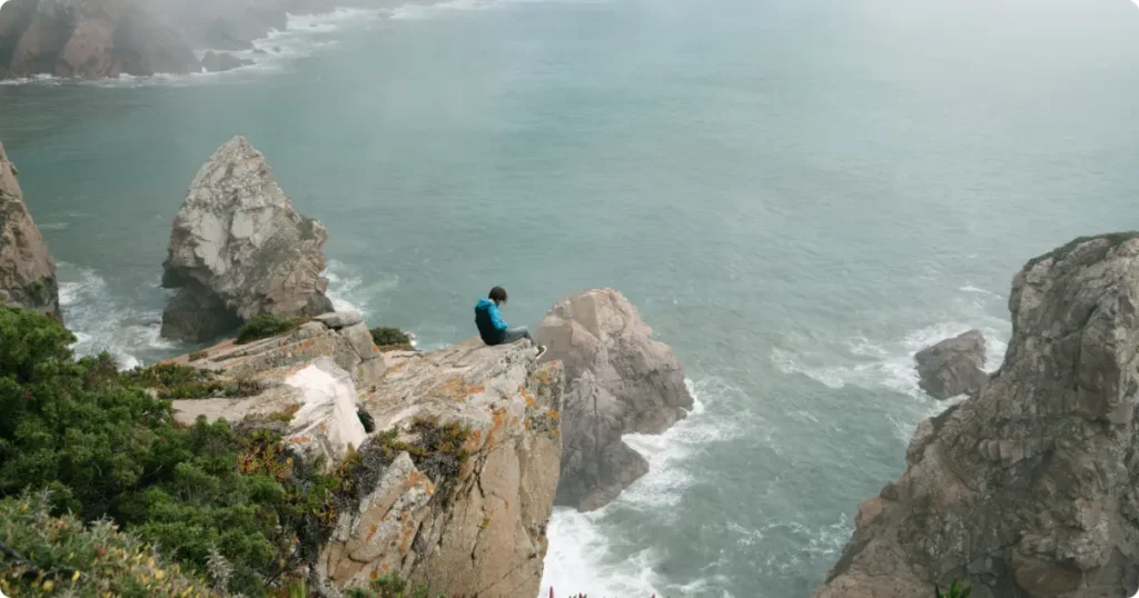 Hiker adjusting waterproof rain jacket hood on exposed coastal cliff trail in heavy mist