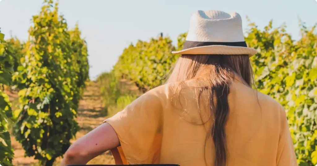Woman in smart casual outfit walking through autumn vineyard rows at golden hour